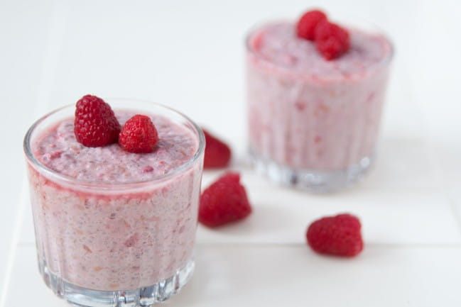 Two glasses filled with raspberry chia seed pudding topped with raspberries.