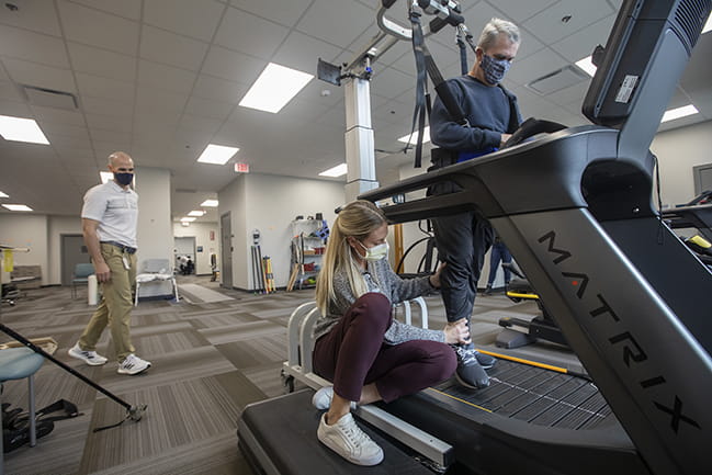 Man on treadmill receives therapy assistance in open, spacious clinic